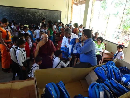 Children in a classroom receiving a blue backpack each