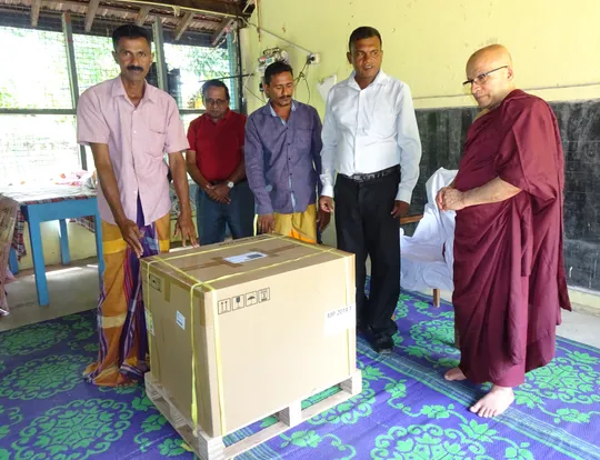 Five people, one of whom is a Buddhist monk gathered around a large cardboard box