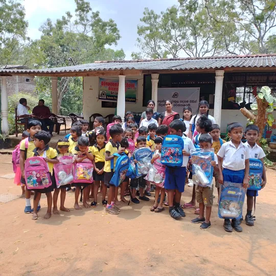 A group of schoolchildren holding up a backpack each. Some children are holding a pink backpack, whereas the others have a blue backpack.